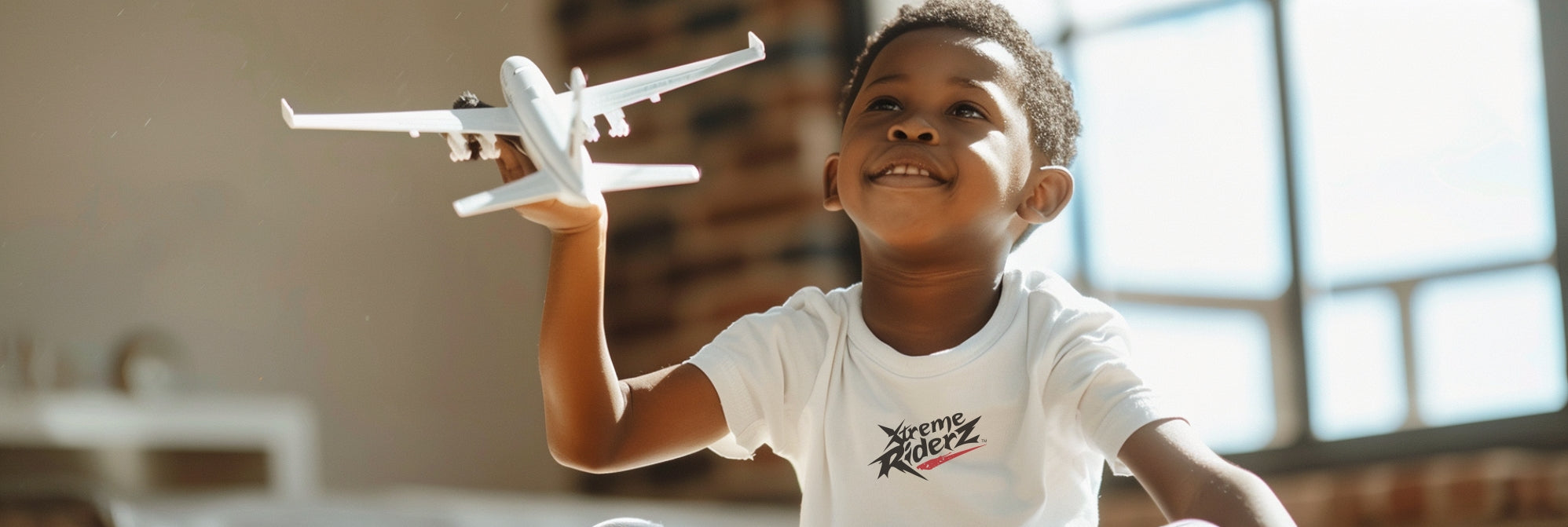African American boy plays with a toy plane. Wears a white t-shirt with the Xreme Riderz logo on it.